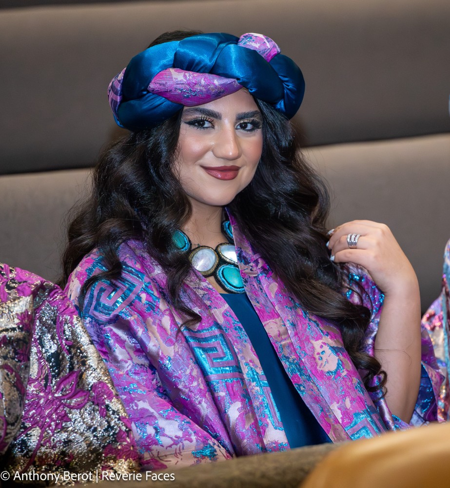 Model wearing a blue and purple headwrap and colourful textiles at a Toronto fashion show.