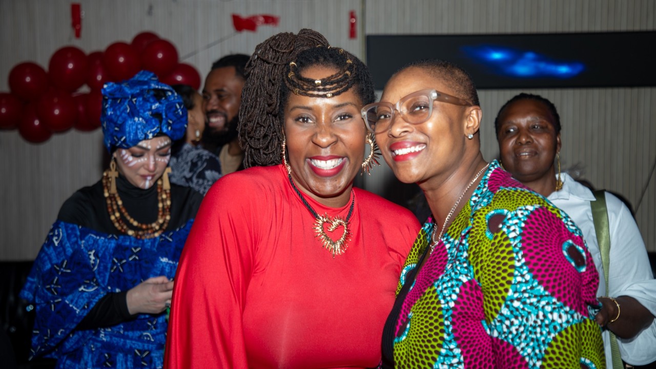 Two guests smiling together in a red outfit and colourful patterned clothing.